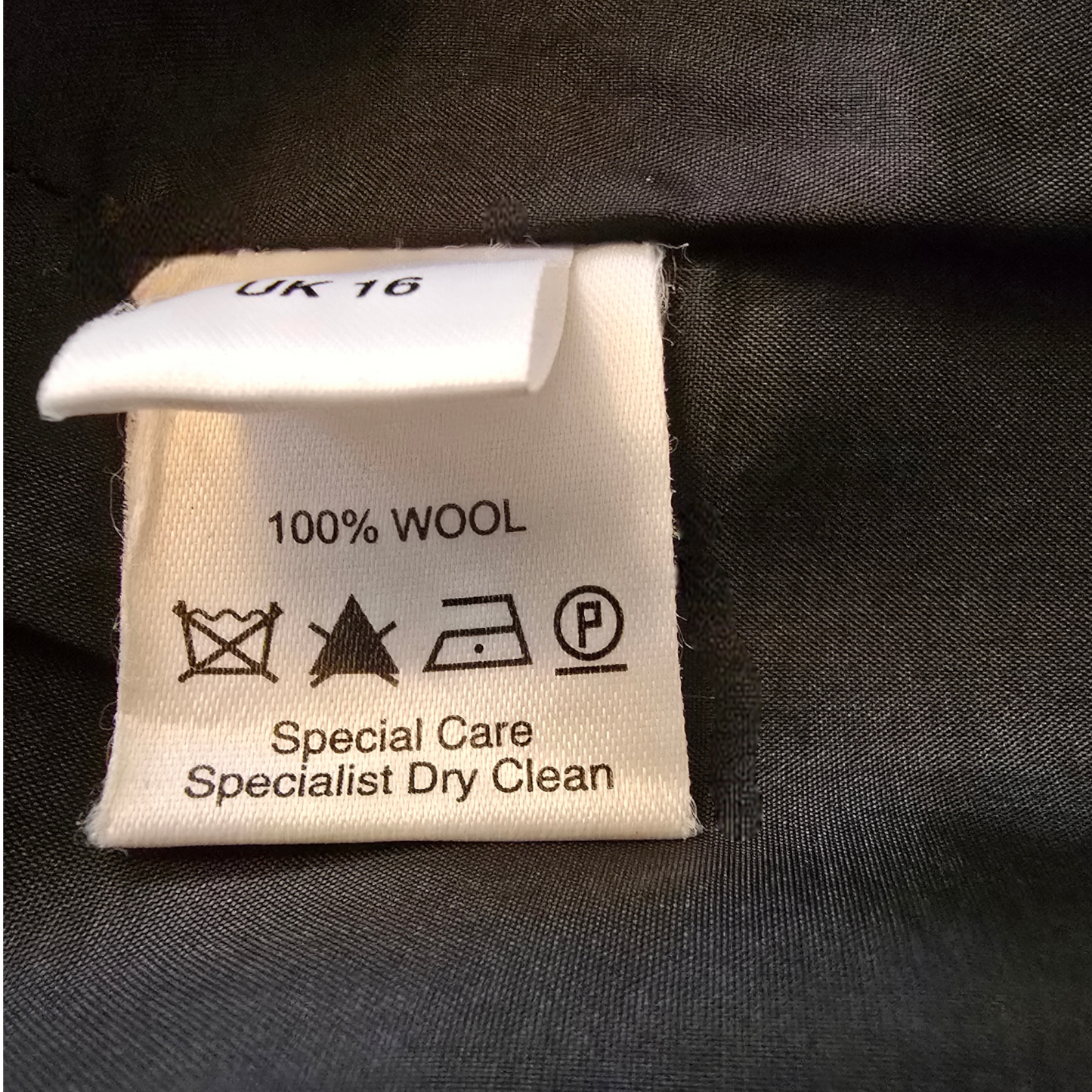 Clothing label with wool content and care instructions on a dark fabric background