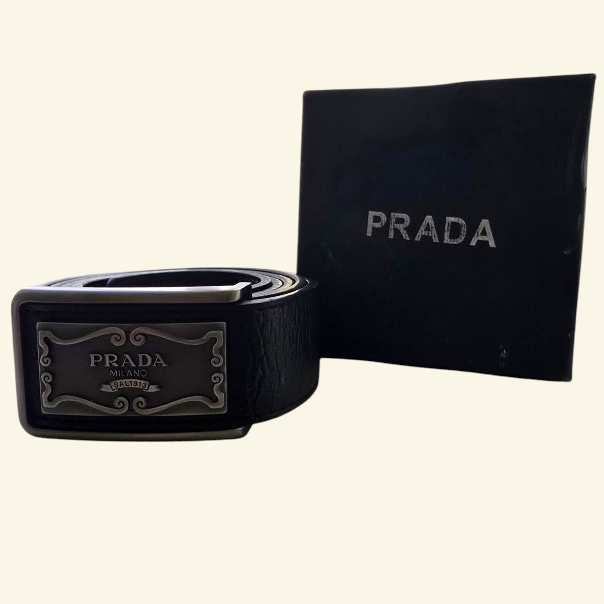 Black Prada belt with silver buckle and Prada logo box on a beige background