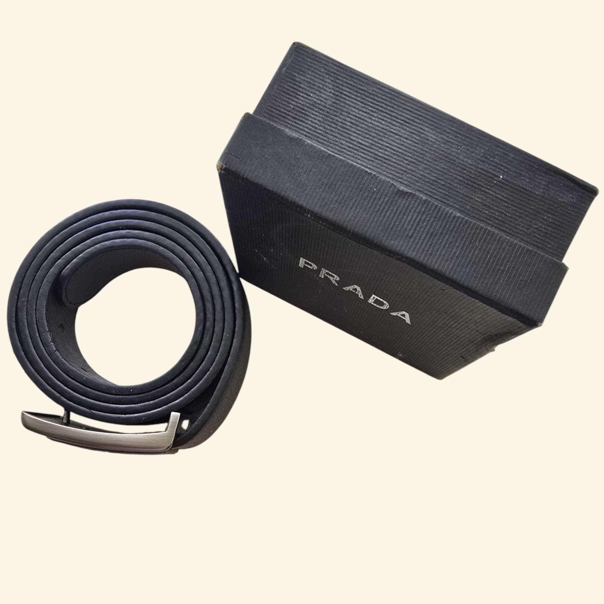 Black Prada belt with a matching box on a beige background