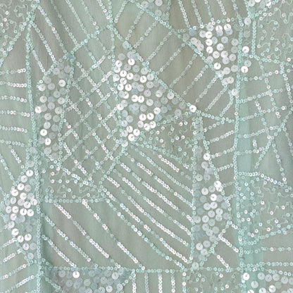 Close-up of a fabric with a geometric pattern and sequins on a light green background