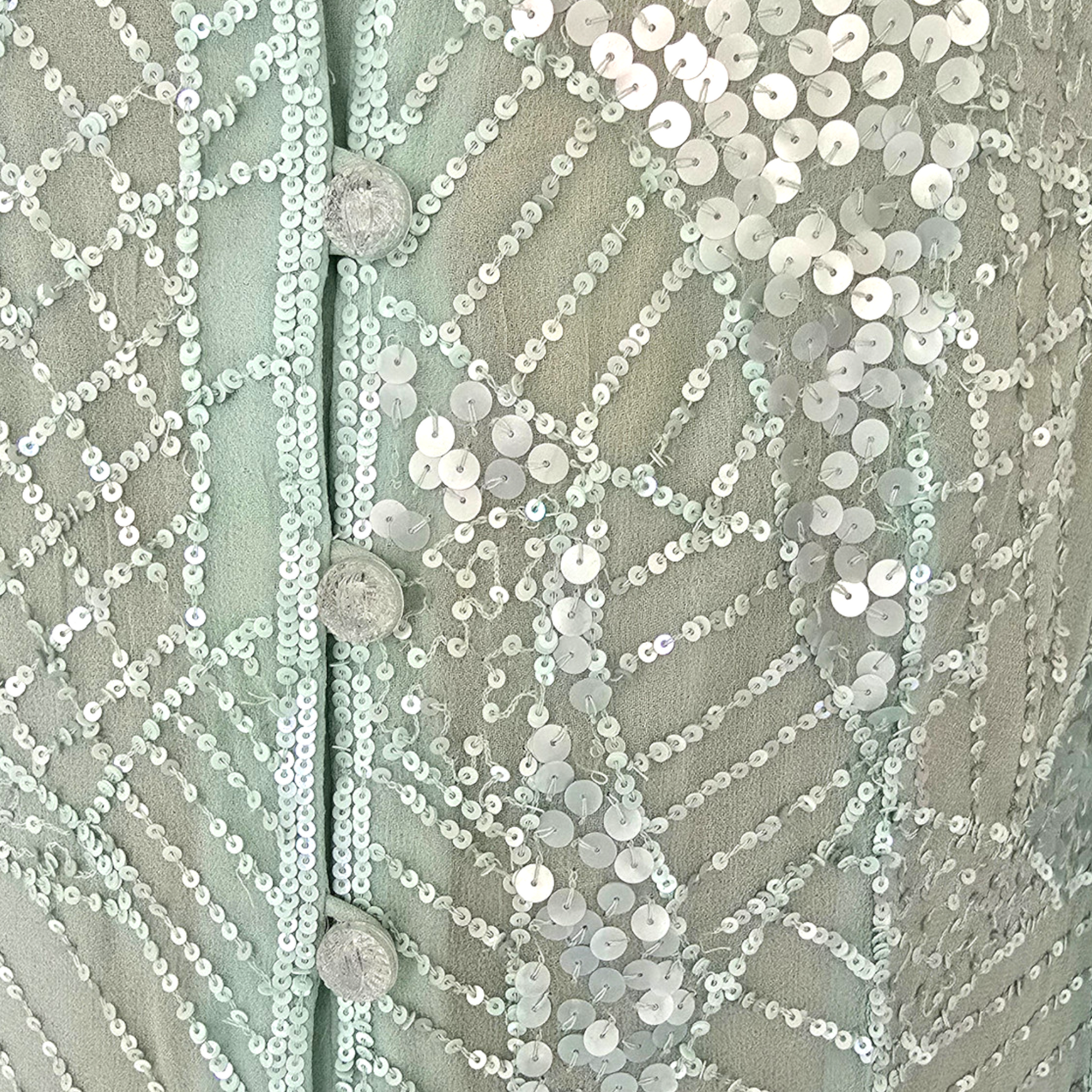 Close-up of a textured fabric with sequins and buttons on a light green background