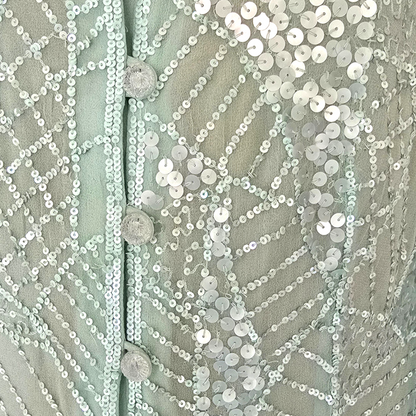 Close-up of a textured fabric with sequins and buttons on a light green background