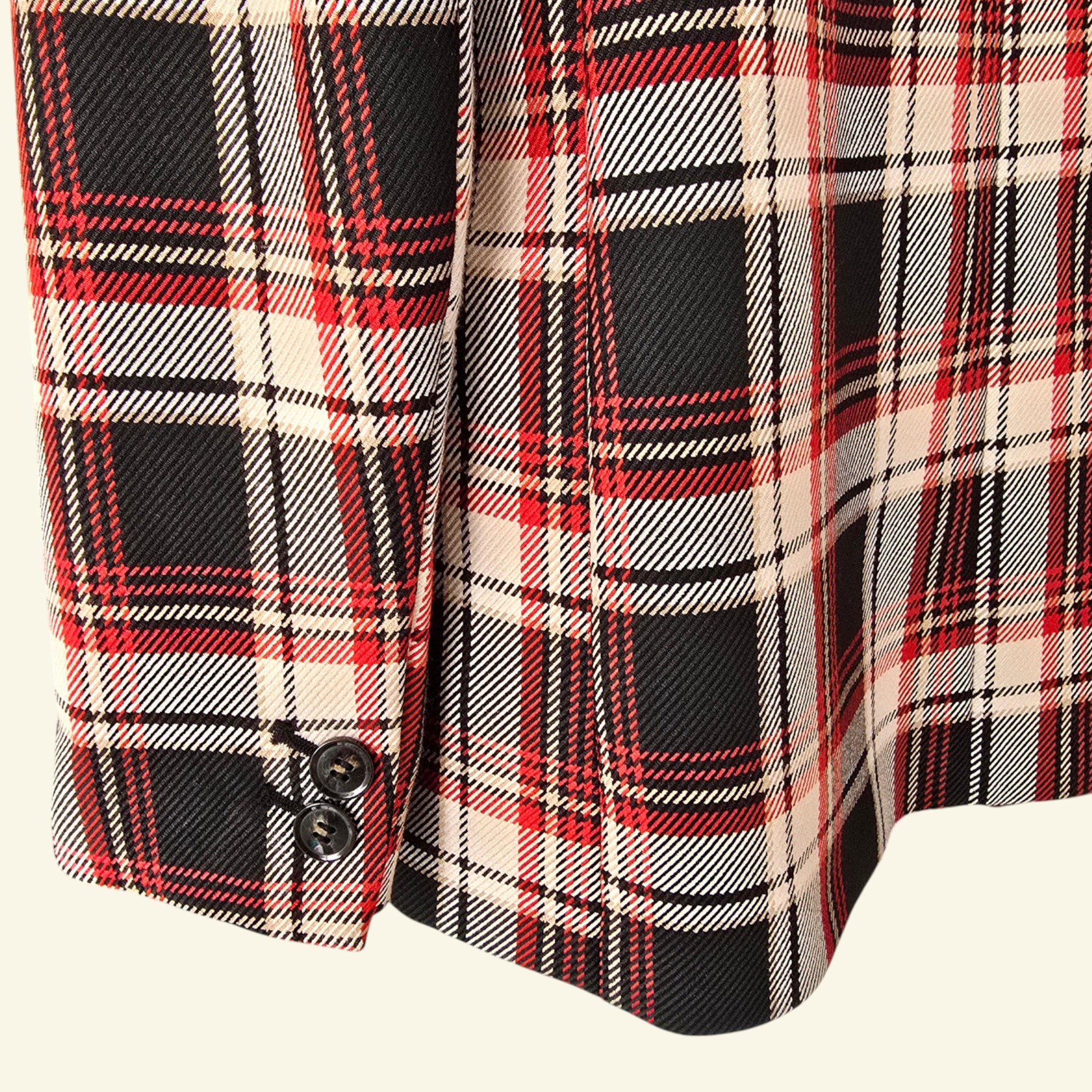 Close-up of a plaid fabric with red, black, and beige colors on a white background.