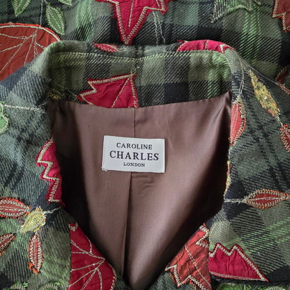 Close-up of a  jacket collar showing a white label that reads 'CAROLINE CHARLES LONDON' on a brown lining, with a green and black plaid and red floral quilted pattern visible around the collar.