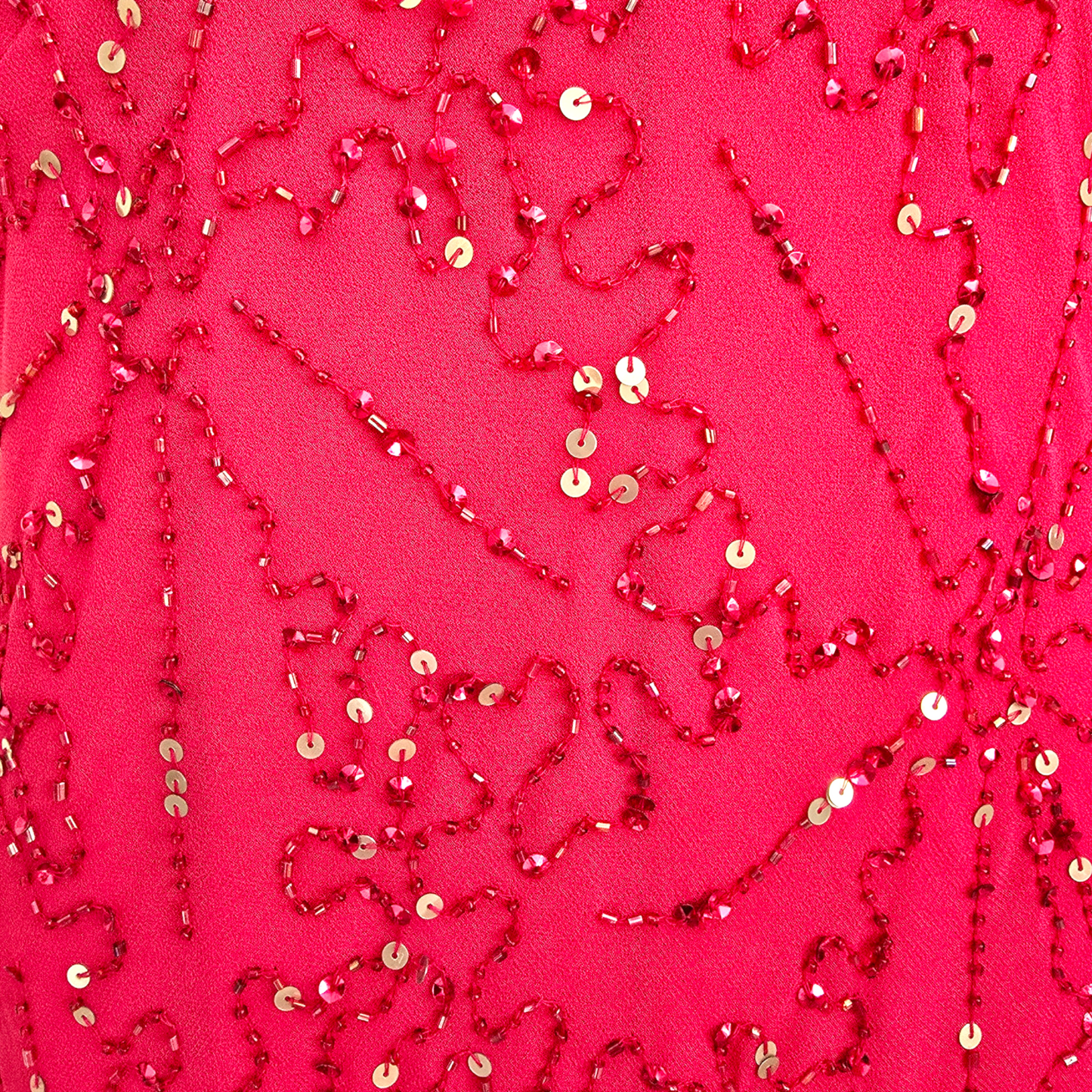 A close-up of a bright pink fabric decorated with red beaded sequin patterns and scattered gold sequins.