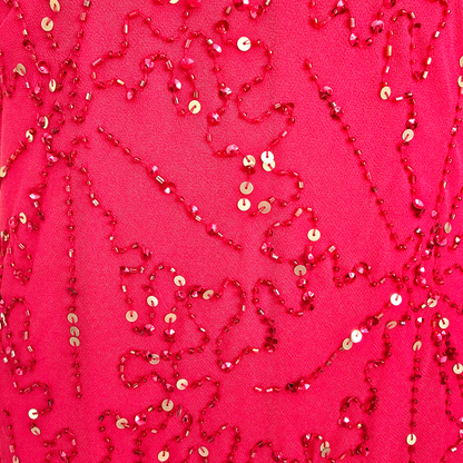 A close-up of a bright pink fabric decorated with red beaded sequin patterns and scattered gold sequins.