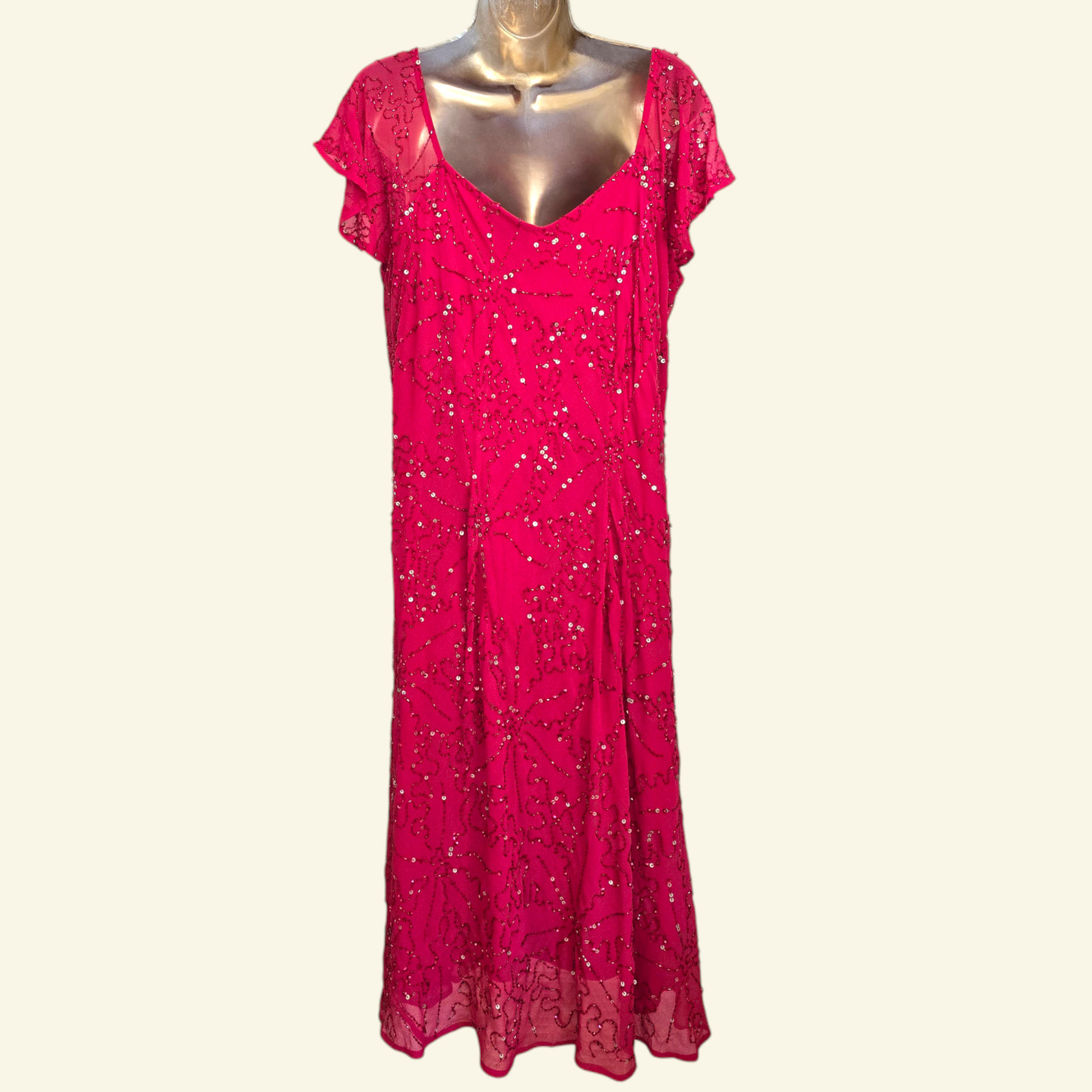 A bright pink dress with short flutter sleeves,  and all-over sequin embellishment, displayed on a metallic mannequin against a light cream background.