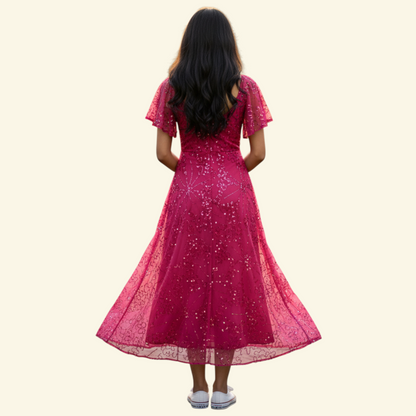 A woman viewed from behind wearing a bright pink sequined midi dress with short flutter sleeves and a flared skirt, standing against a plain light beige background.