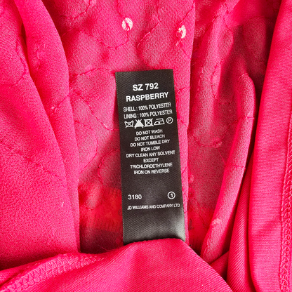 Close-up of a bright pink garment interior with a black sewn-in size and care label reading SZ 792 RASPBERRY, plus fabric texture and stitching visible.
