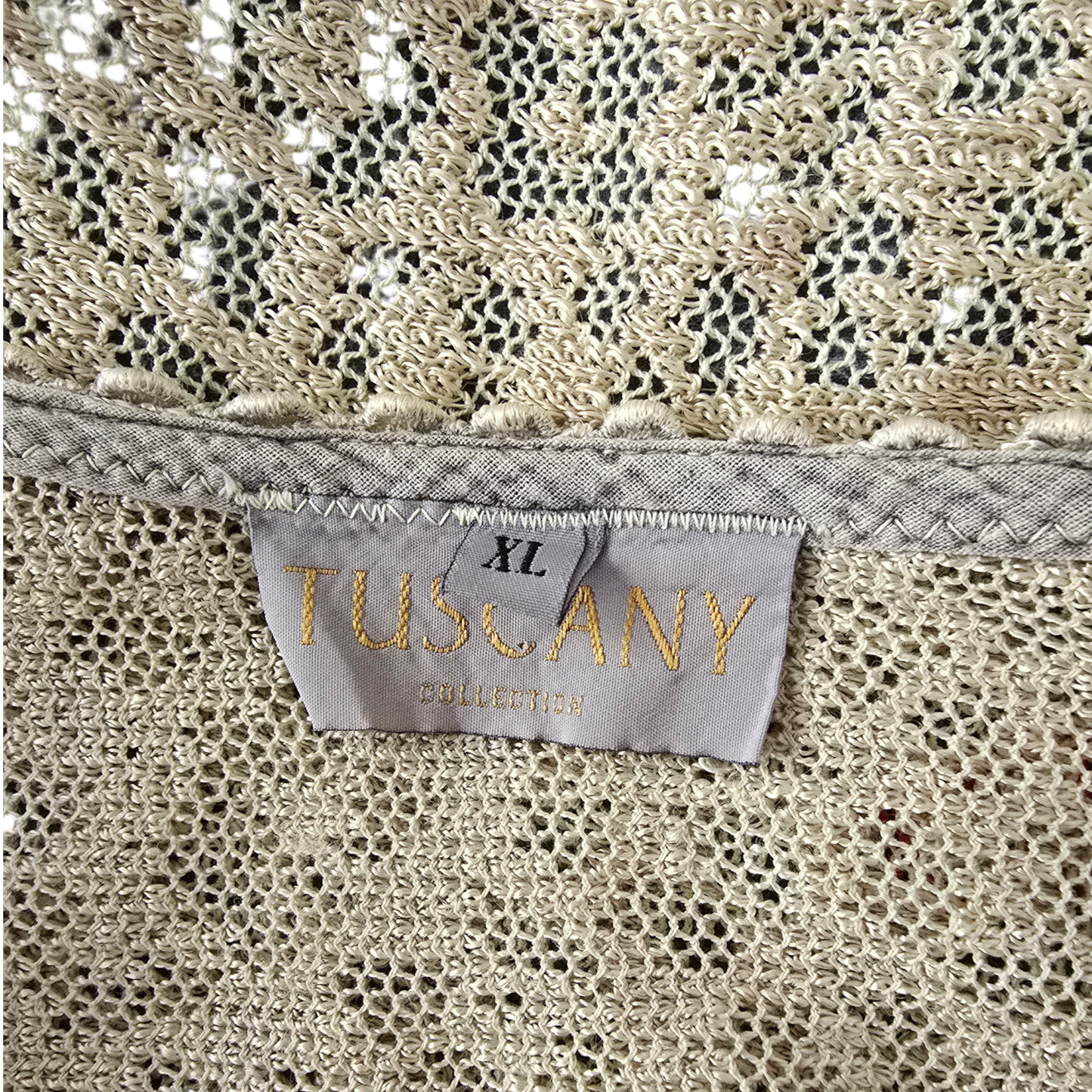 Close-up of a beige fabric with size tag reading TUSCANY COLLECTION and XL, showing the interior neckline and textured lace-like fabric.