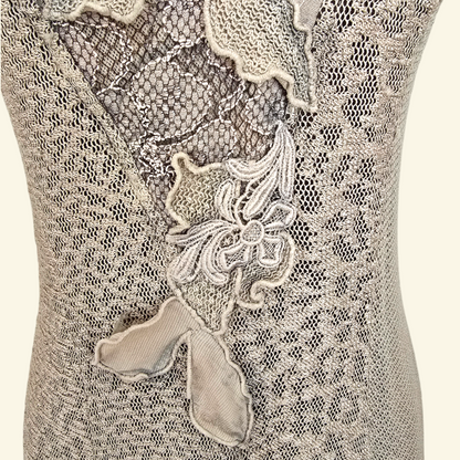 Close-up of a beige lace garment with floral applique and mesh detailing on a mannequin torso.