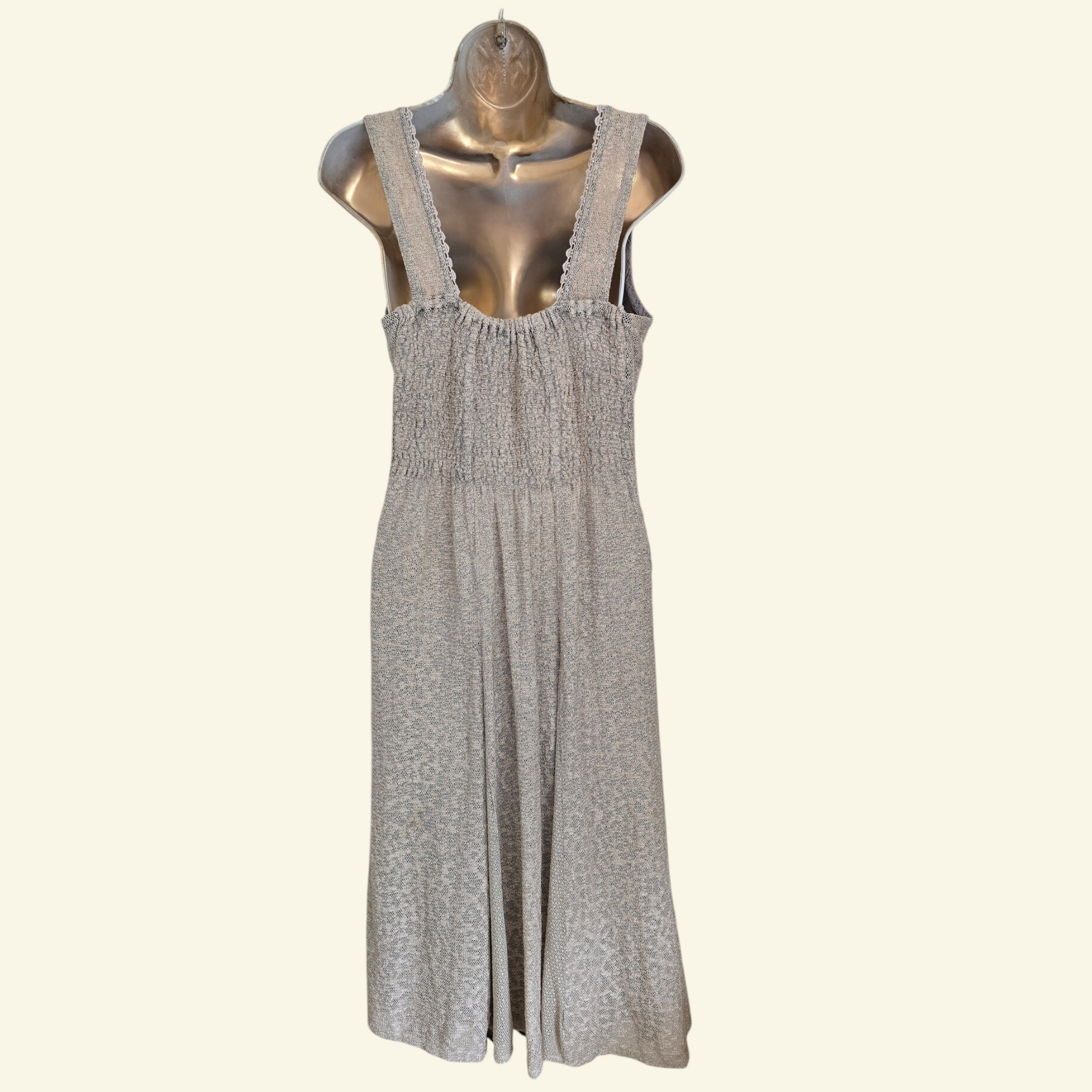 A sleeveless light beige dress with a, displayed on a metallic mannequin against a solid cream background.
