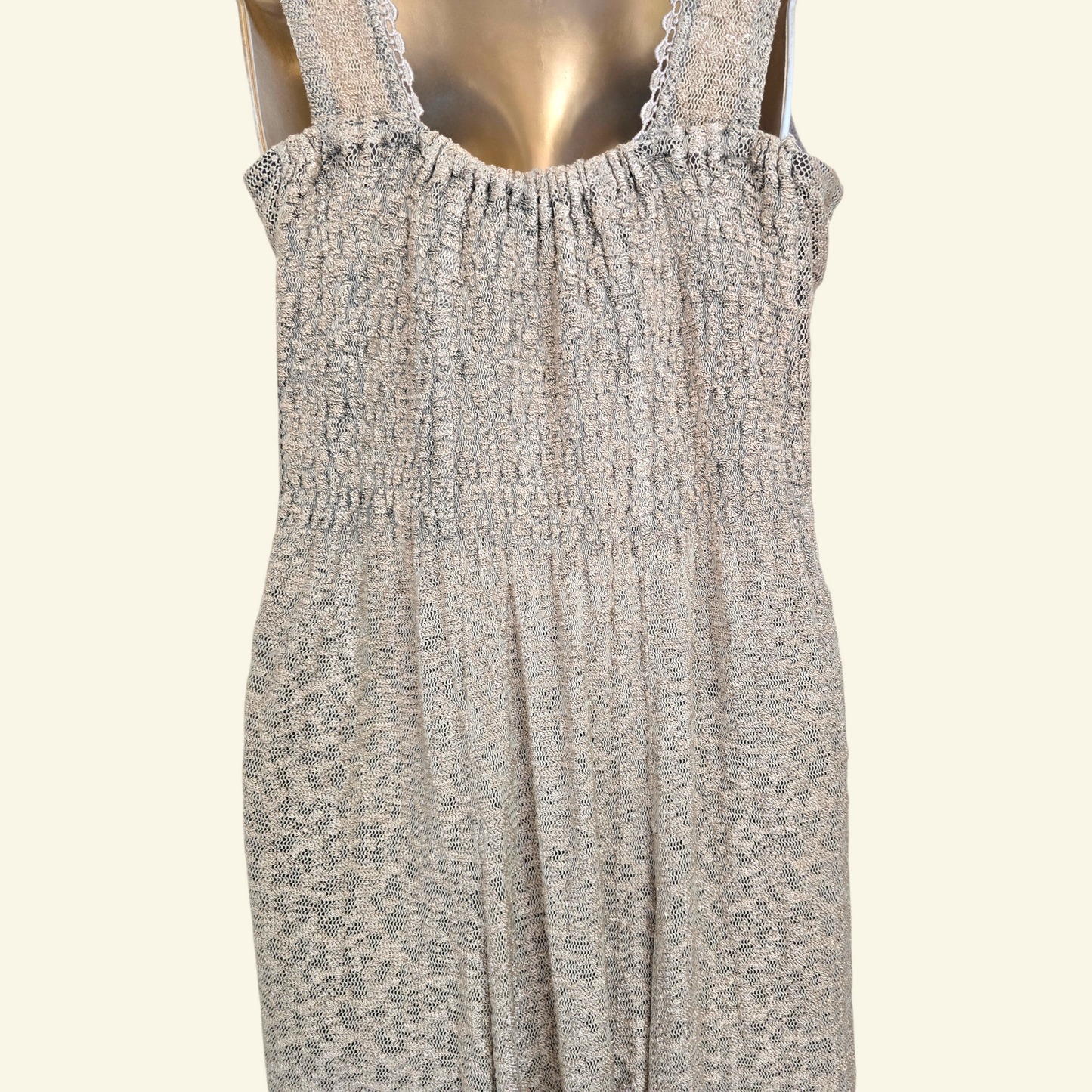 Back view of sleeveless smocked dress with a beige pattern, displayed on a metallic gold mannequin against a light cream background.