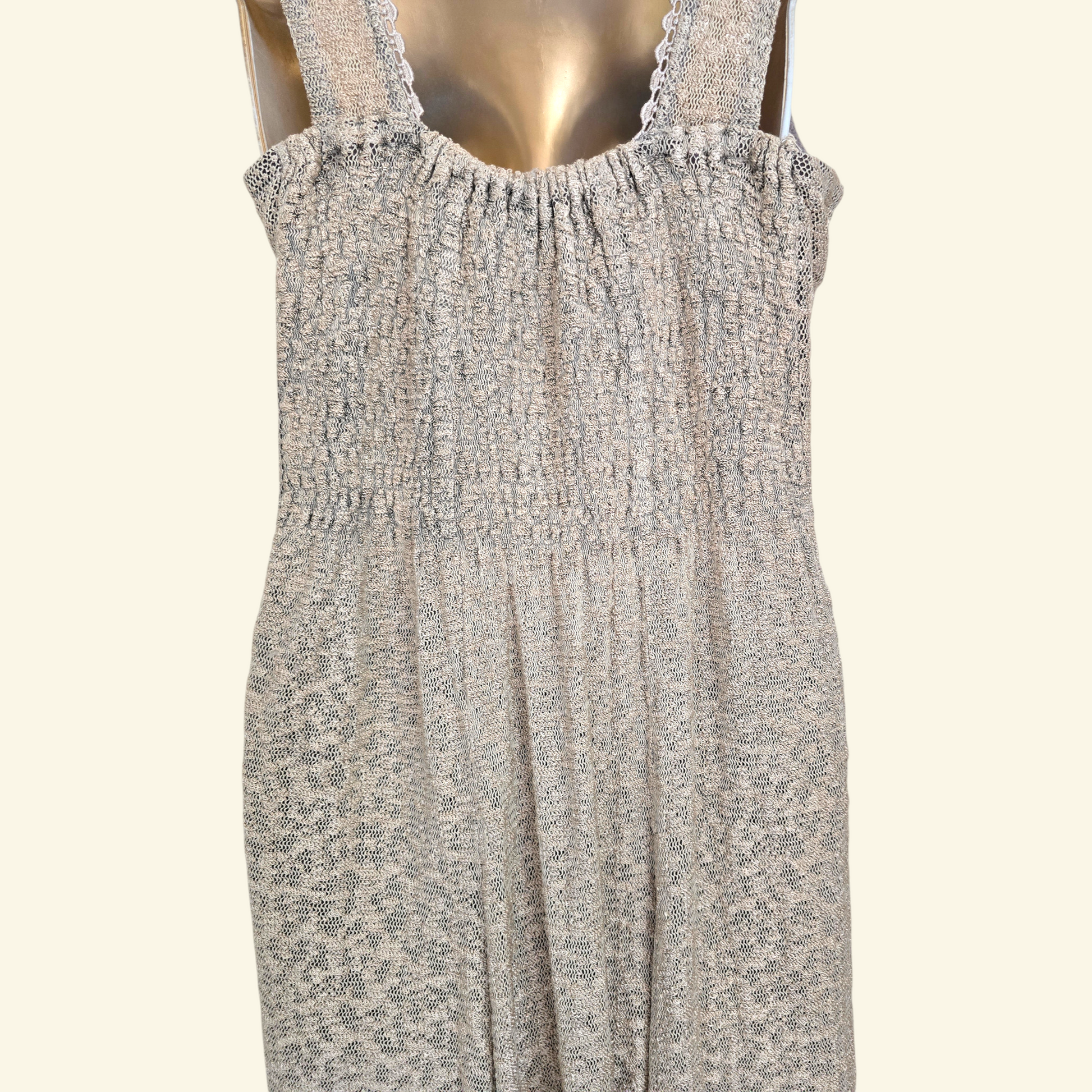 Back view of sleeveless smocked dress with a beige pattern, displayed on a metallic gold mannequin against a light cream background.
