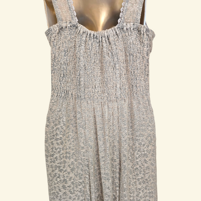 Back view of sleeveless smocked dress with a beige pattern, displayed on a metallic gold mannequin against a light cream background.