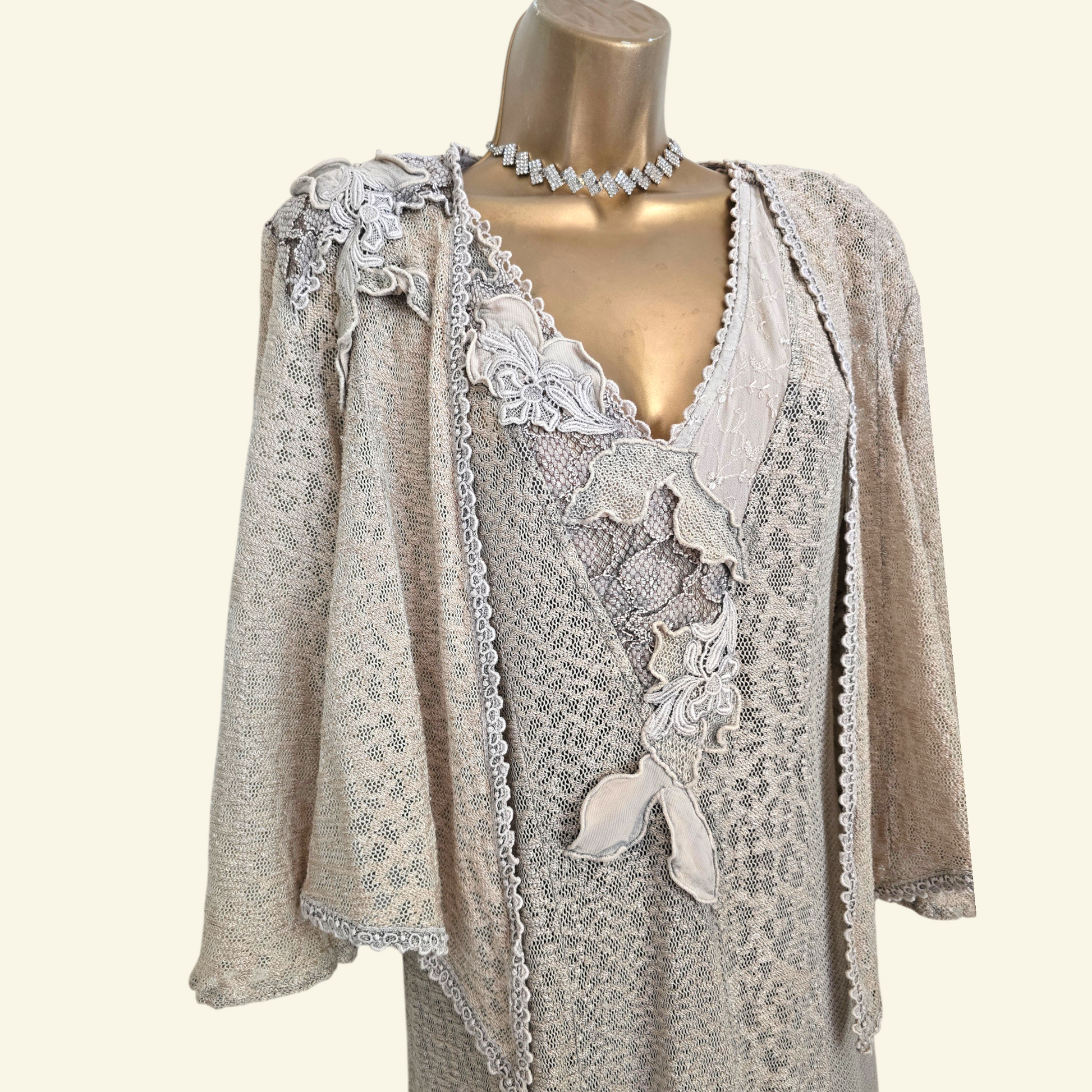 A beige patterned jacket with lace appliques and ruffles, displayed on a gold mannequin torso against a cream background.