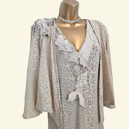A beige patterned jacket with lace appliques and ruffles, displayed on a gold mannequin torso against a cream background.