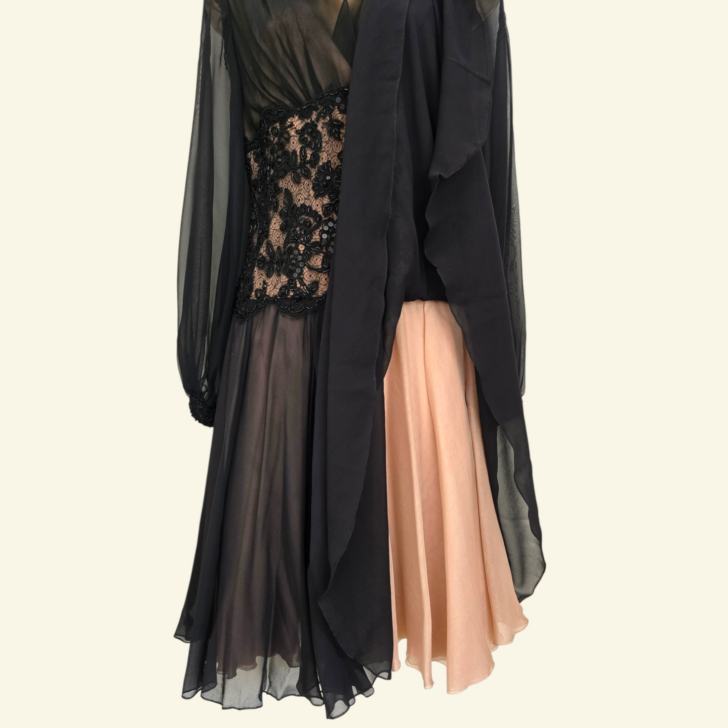 A long black sheer overlay dress with a black lace bodice, layered over a peach-colored chiffon skirt, shown against a plain light beige background.