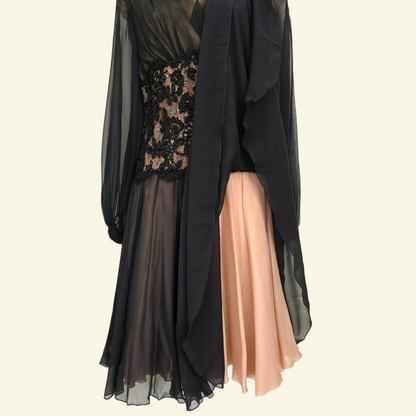 A long black sheer overlay dress with a black lace bodice, layered over a peach-colored chiffon skirt, shown against a plain light beige background.