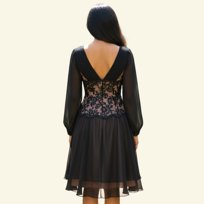 A woman viewed from the back wearing a black long-sleeve dress with sheer mesh sleeves, a lace-trimmed open back, and a flowing skirt against a plain light beige background.