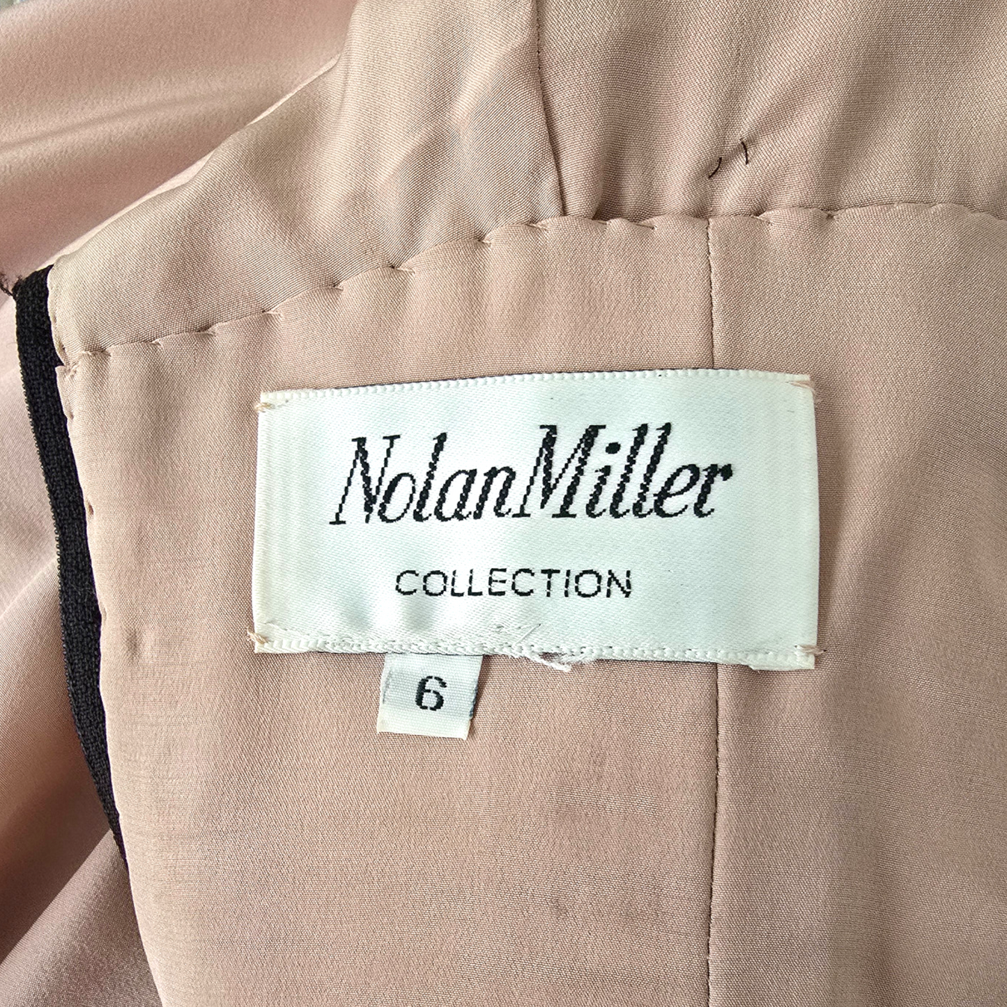 Close-up of a light blush pink garment with a visible white fabric label reading 'Nolan Miller COLLECTION' and a small size tag marked '6'.
