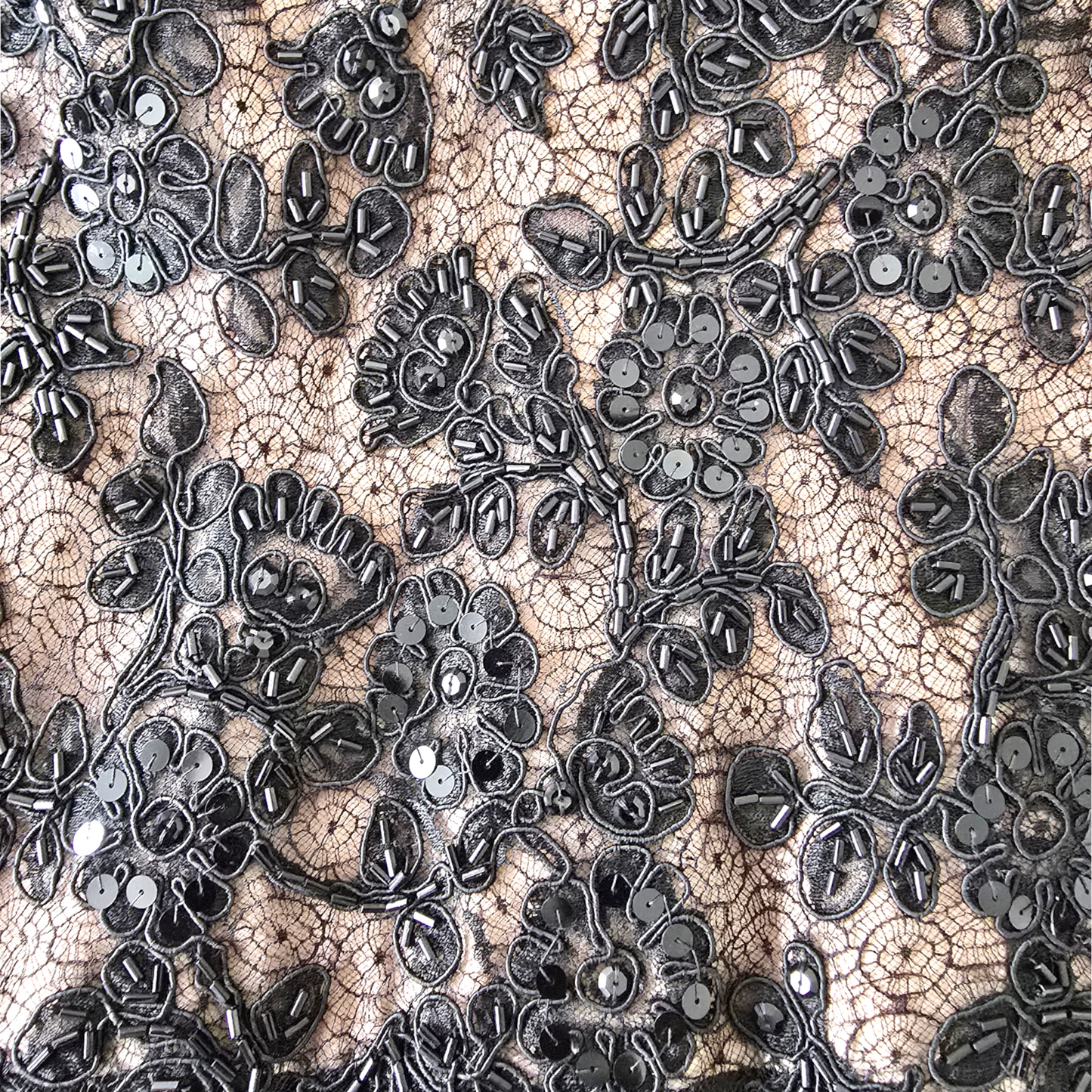 Black floral lace fabric with sequins and bead embroidery over a beige mesh background.