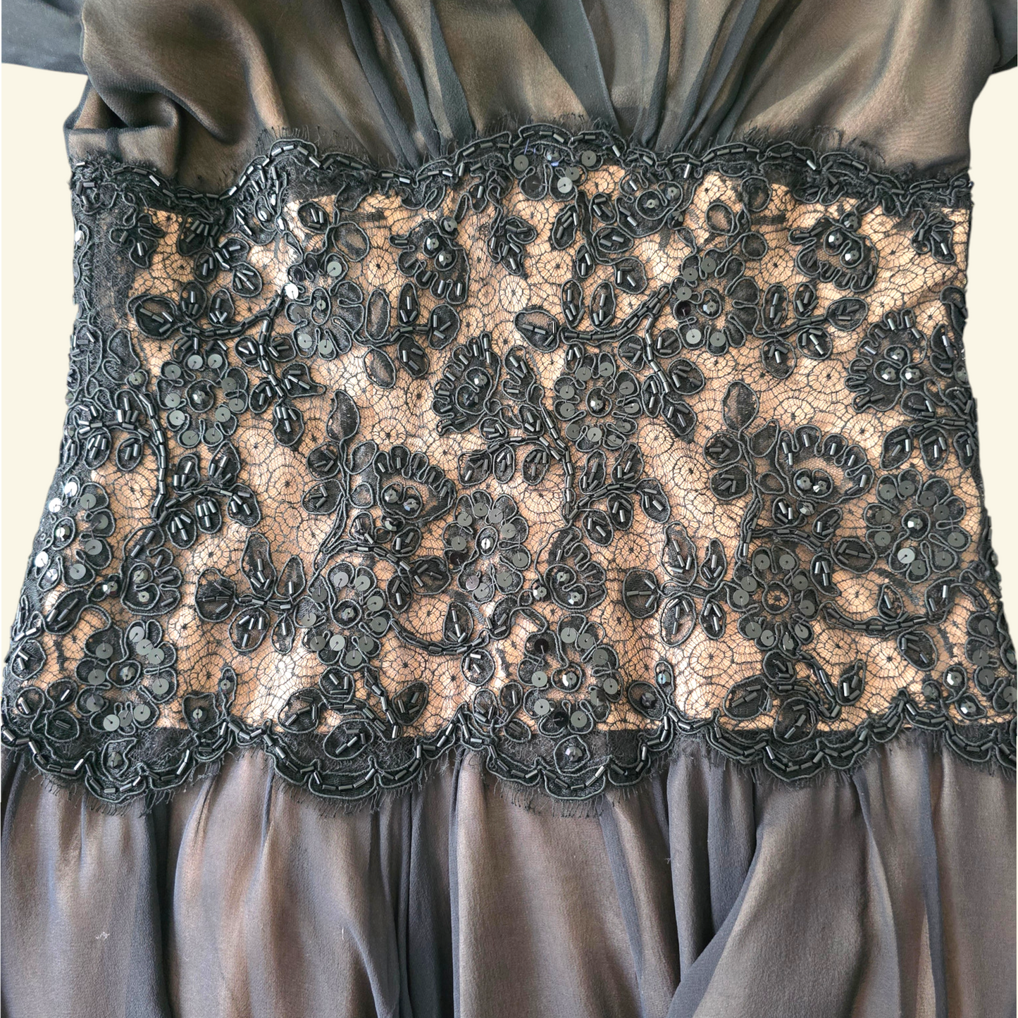 Close-up of a black satin dress with a wide black floral lace corset waistband featuring bead embellishments.