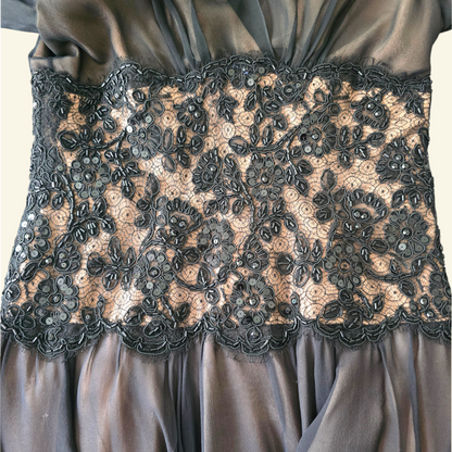 Close-up of a black satin dress with a wide black floral lace corset waistband featuring bead embellishments.