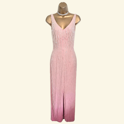 A sleeveless pink maxi dress with a beaded fringe texture, displayed on a gold mannequin torso against a light cream background.