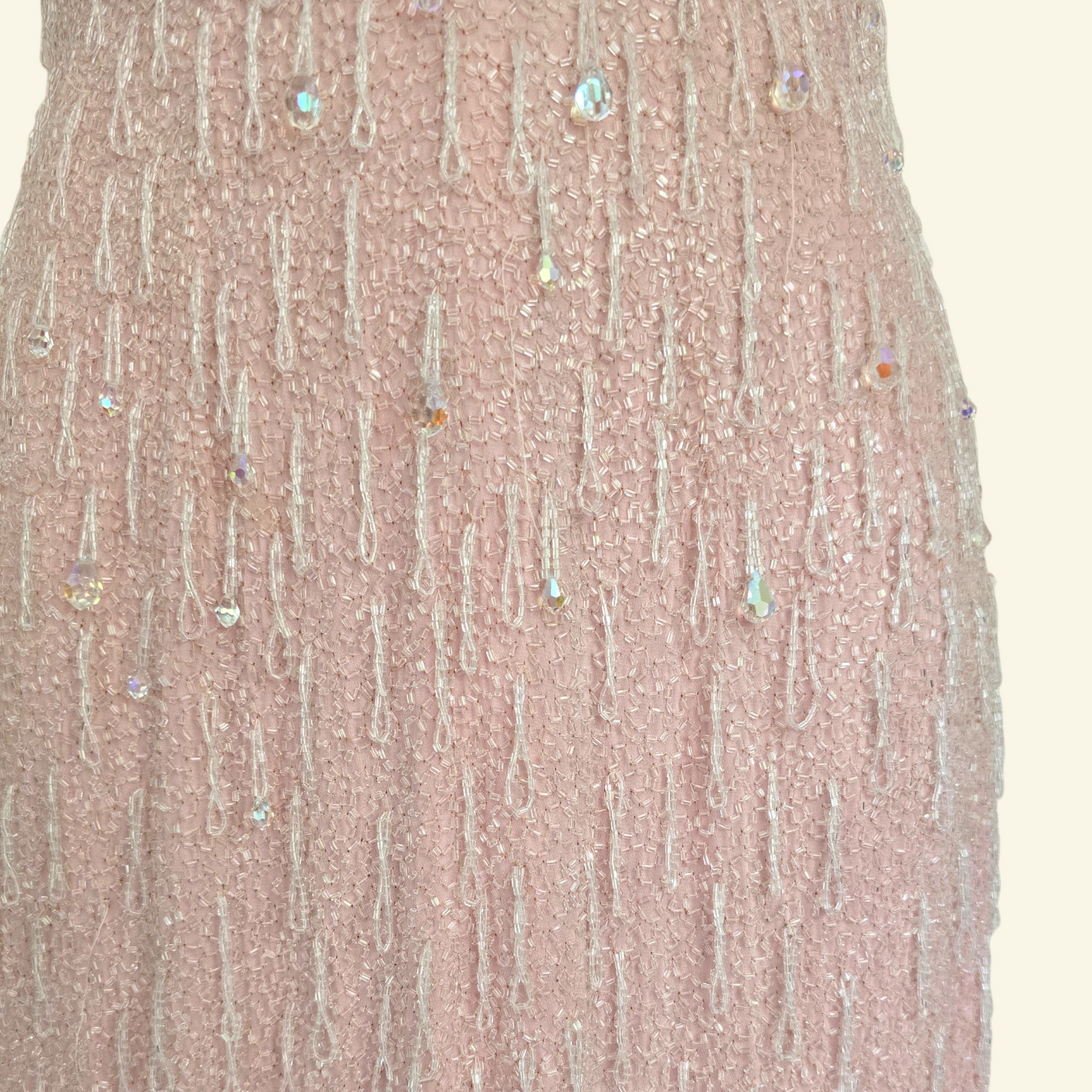 Close up of hand beaded detail on pink dress on beige background