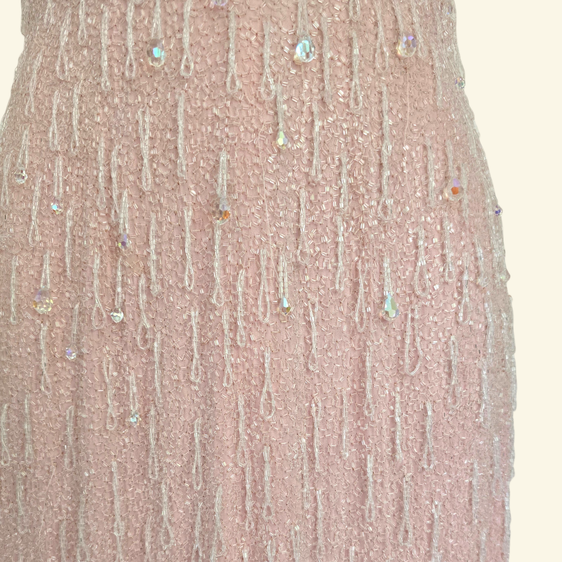 Close up of hand beaded detail on pink dress on beige background