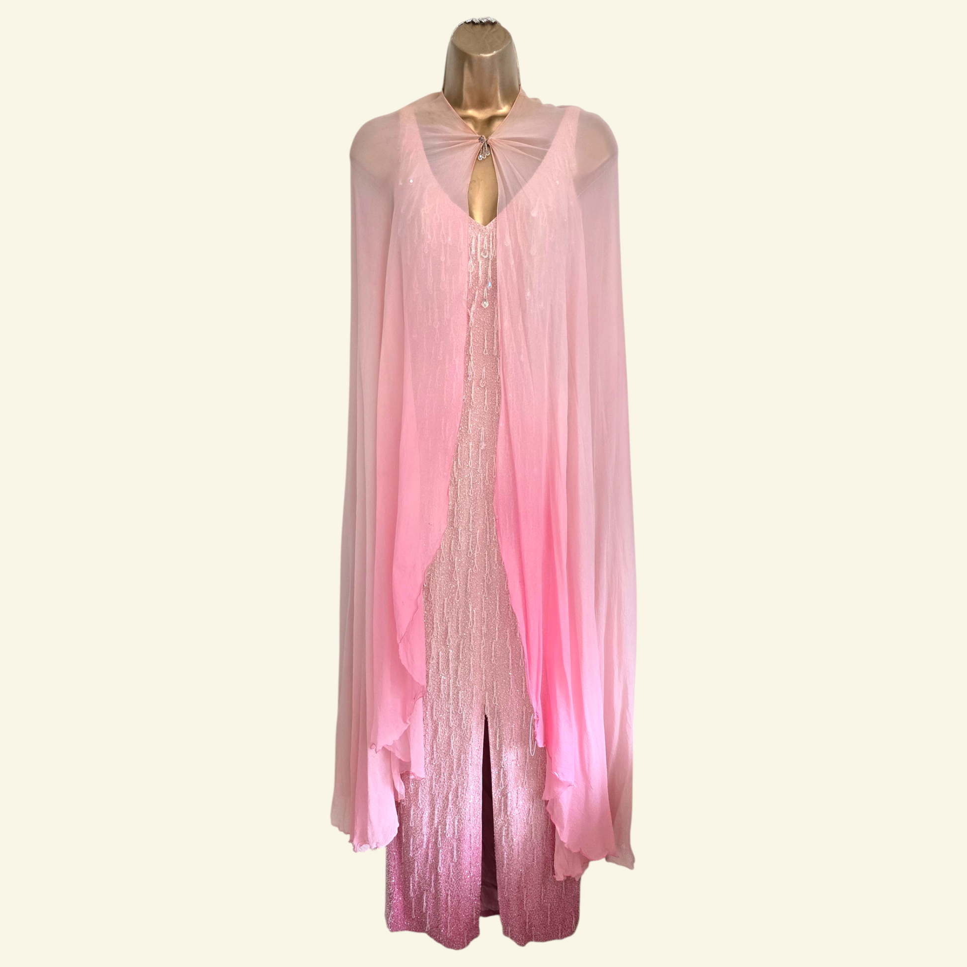 A pink sheer long-sleeve draped cover-up with a tie-neck detail, displayed on a gold mannequin torso against a light cream background.