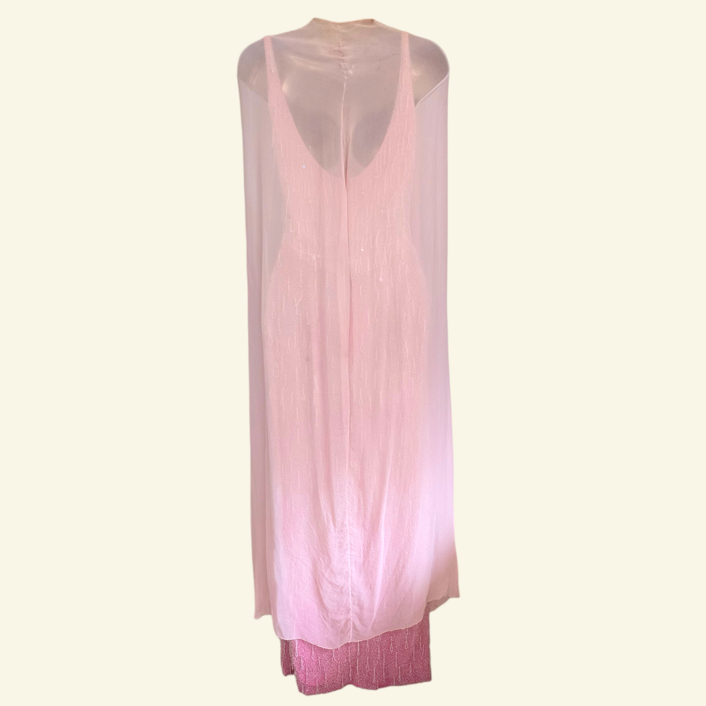 A light pink sleeveless maxi dress with a sheer mesh overlay, displayed on a mannequin against a solid cream background.