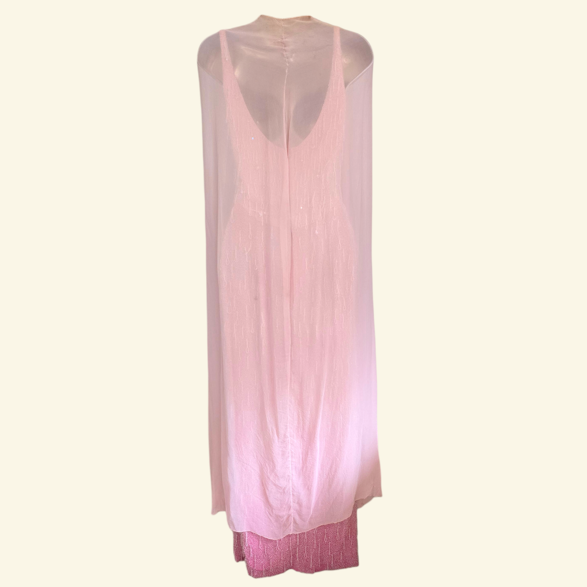 A light pink sleeveless maxi dress with a sheer mesh overlay, displayed on a mannequin against a solid cream background.