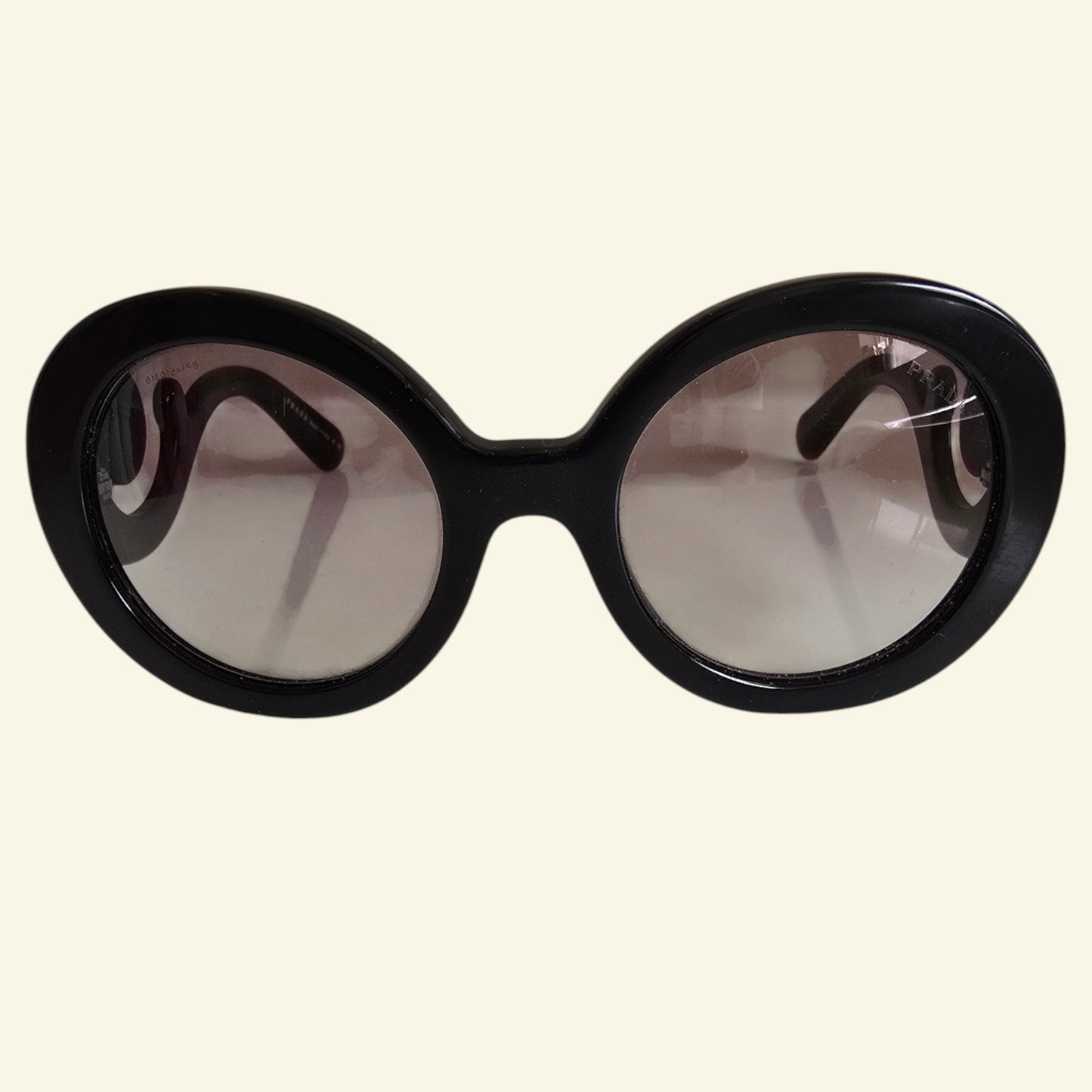 Oversized round sunglasses with a thick black frame and gradient tinted lenses, shown against a solid cream background.