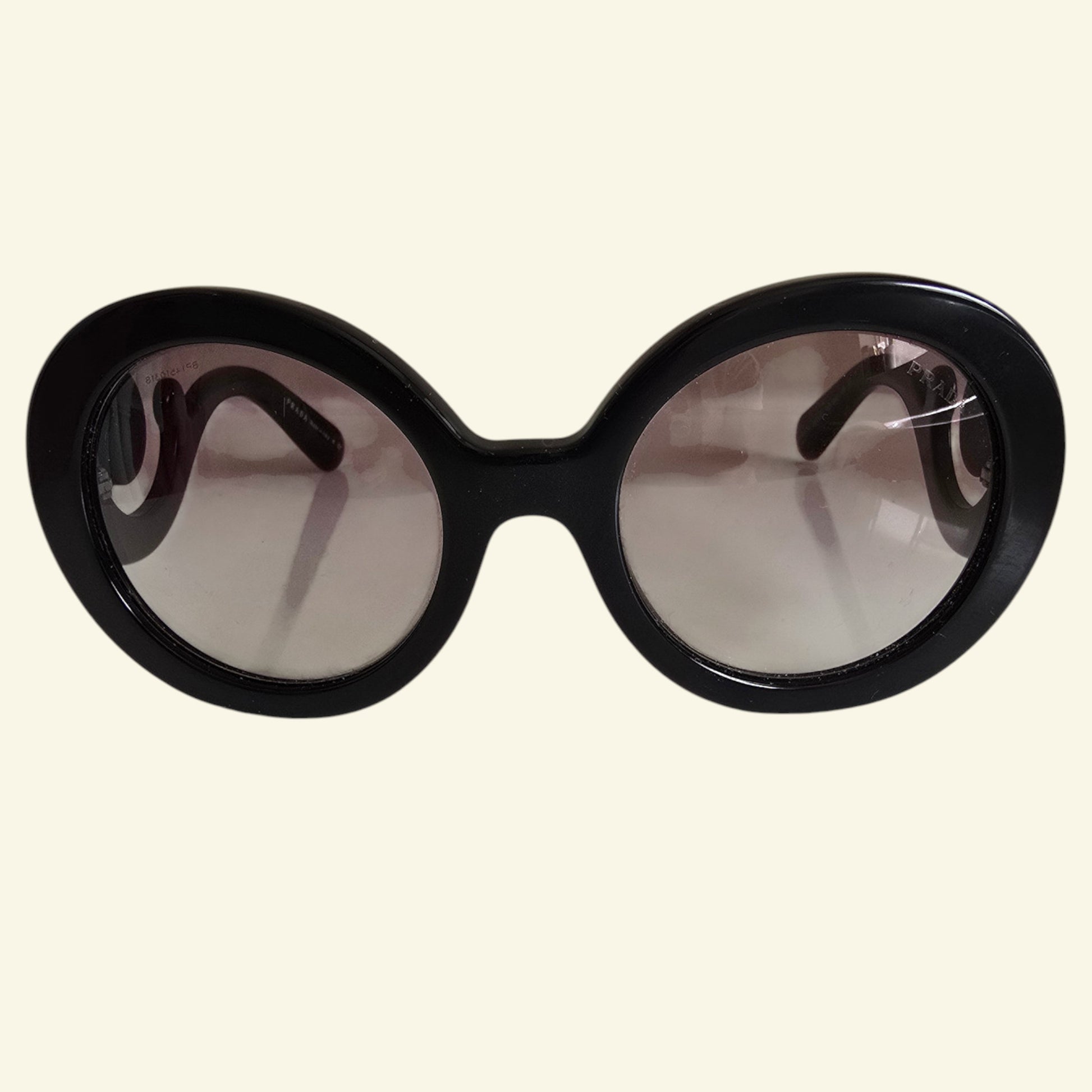 Oversized round sunglasses with a thick black frame and gradient tinted lenses, shown against a solid cream background.