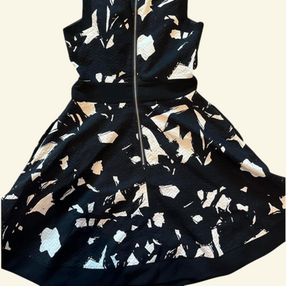 A sleeveless black dress with a textured abstract pattern of beige, white, and light blue shapes, featuring a central front zipper and a matching black waistband.