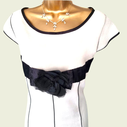 Mannequin wearing a white dress with black accents and a black bow detail on a light green background.