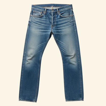 A pair of medium wash blue denim jeans with whiskering and subtle fading on the thighs, presented flat against a solid cream background.