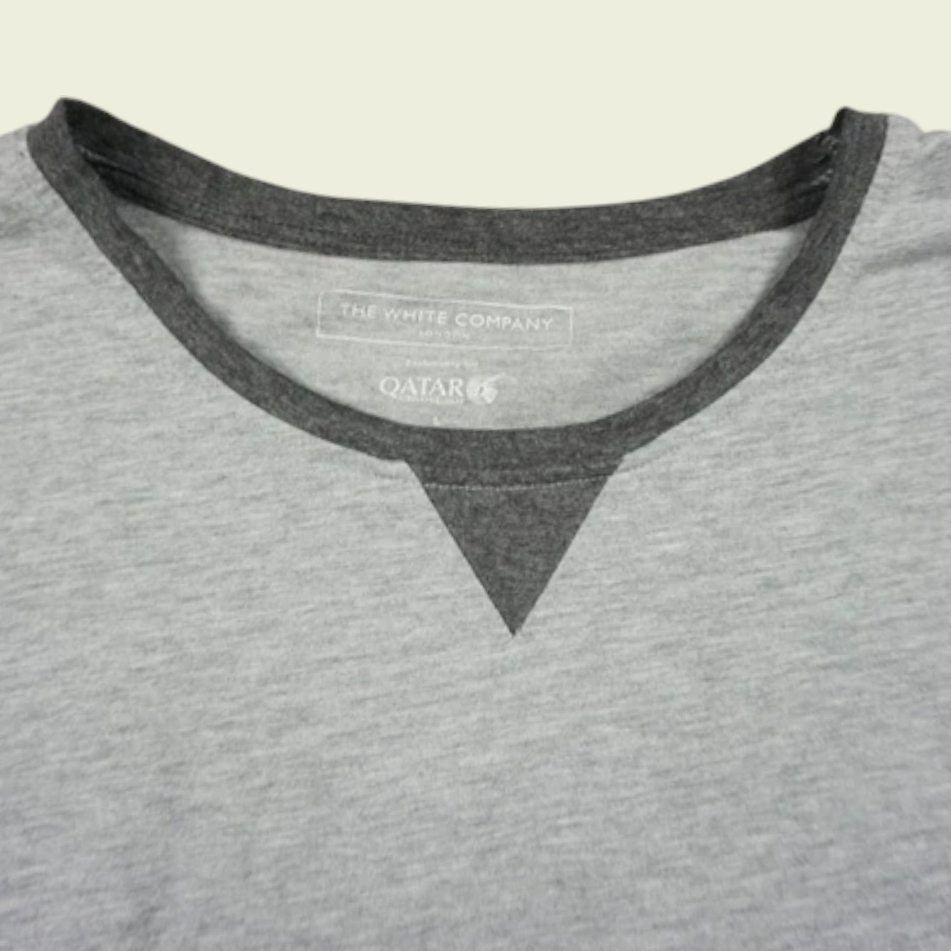 Gray shirt with black trim and visible brand logo on a beige background
