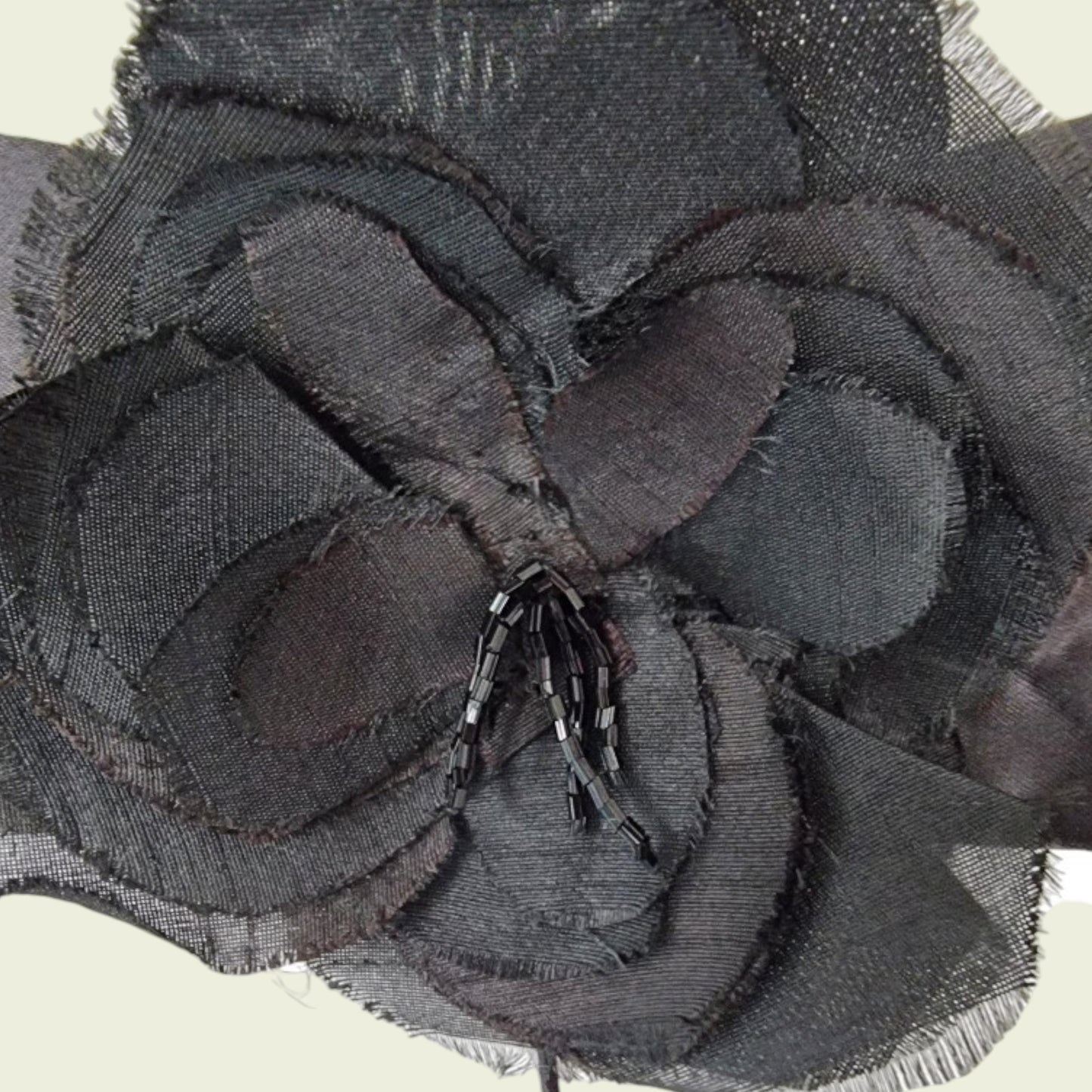 Close-up of a textured black fabric flower with beads on a neutral background