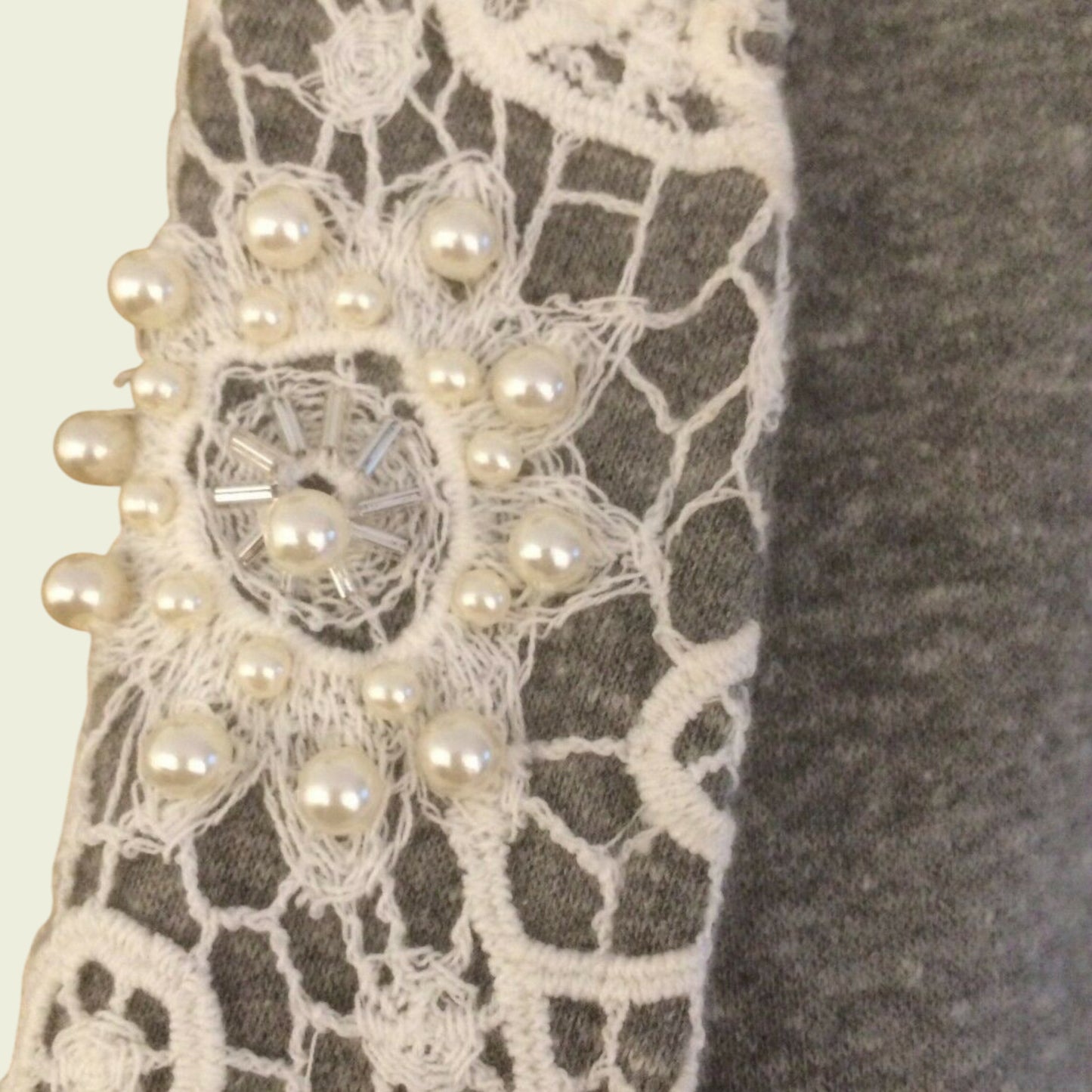Close-up of a lace fabric with pearl embellishments on a neutral background