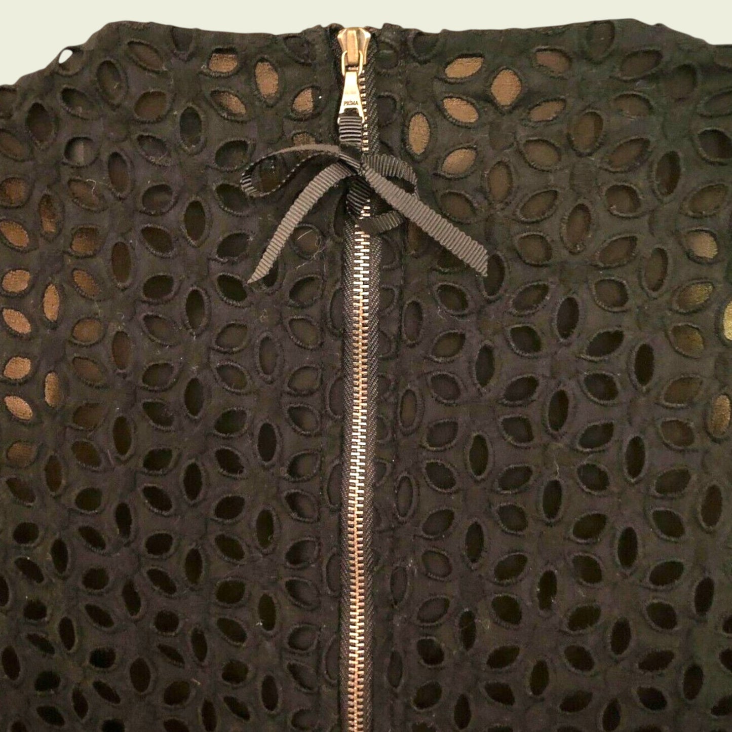 Black textured garment with a gold zipper on a beige background