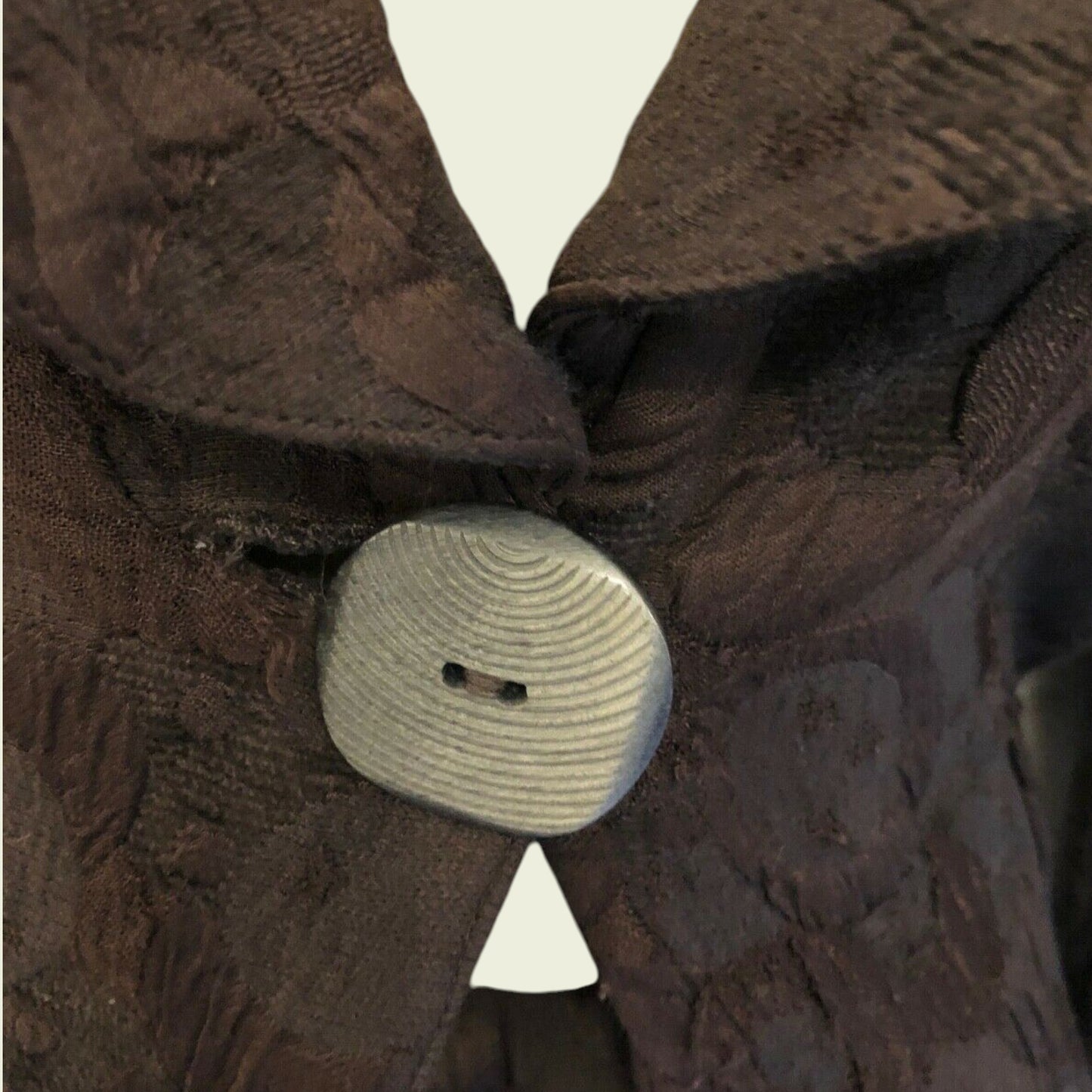 Close-up of a brown textured fabric with a button and white triangle