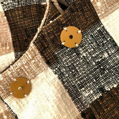 Close-up of a textured fabric with tan buttons on a plaid pattern
