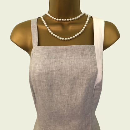 Mannequin wearing a gray apron with a pearl necklace on a light beige background