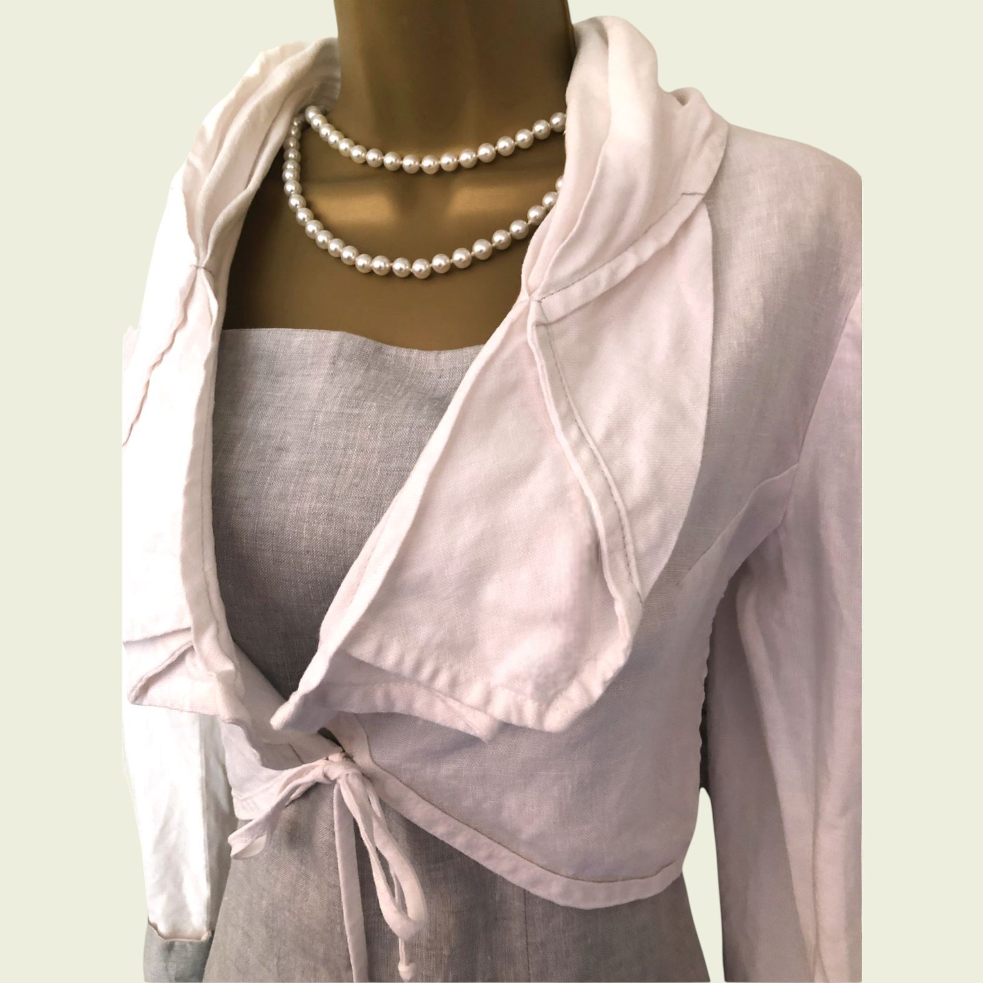 Light pink jacket over a gray dress on a mannequin with a pearl necklace.