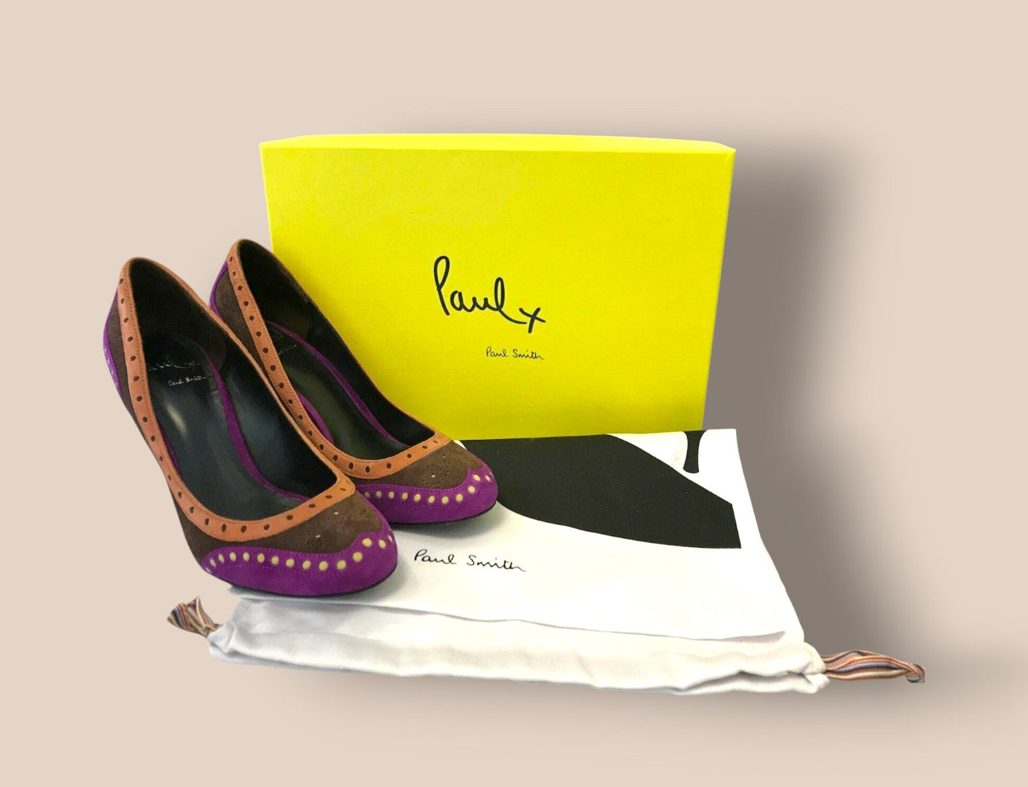 Pair of high-heeled shoes with a yellow box and white bag featuring 'Paul Smith' branding on a beige background.