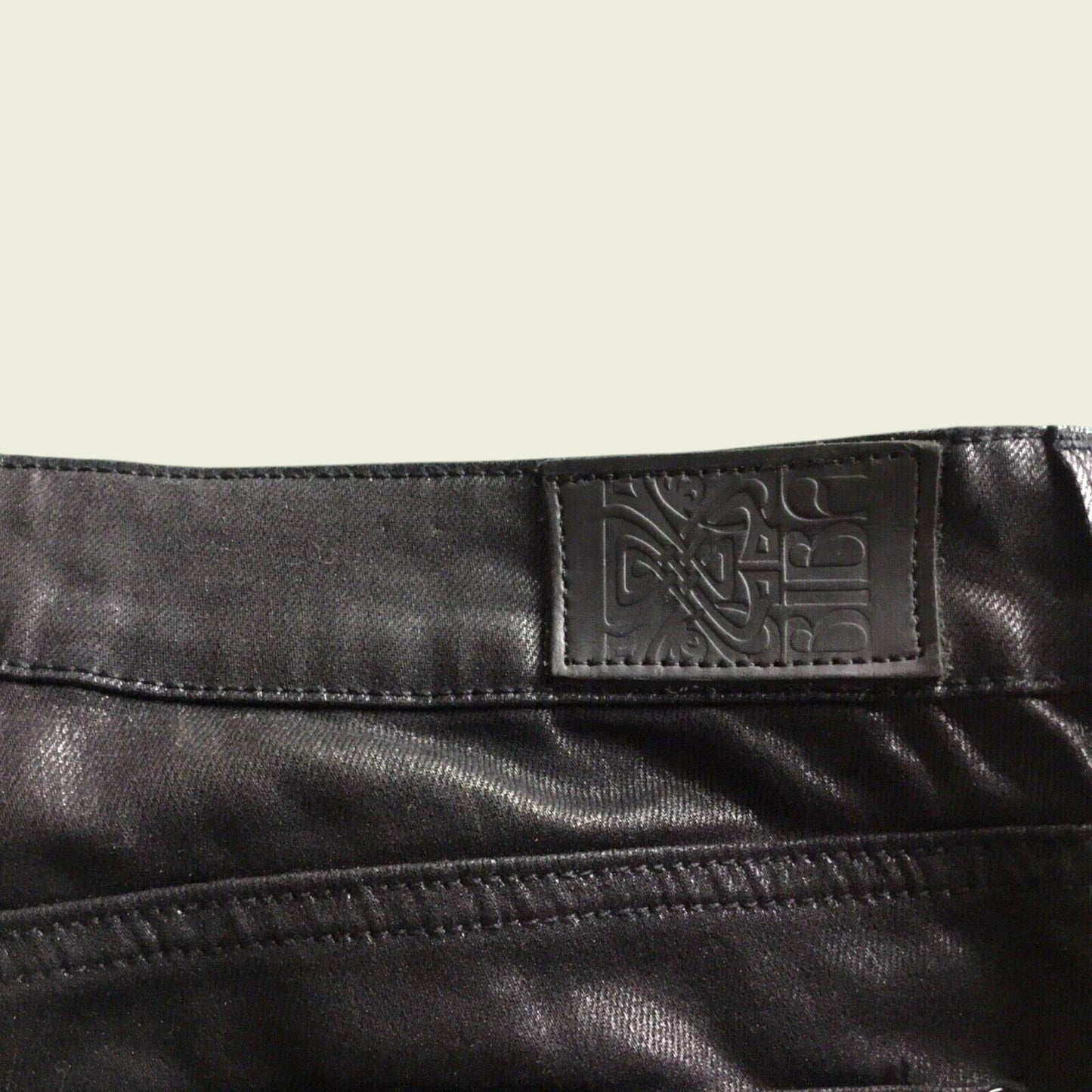 Close-up of a black leather product with a brand label on a beige background
