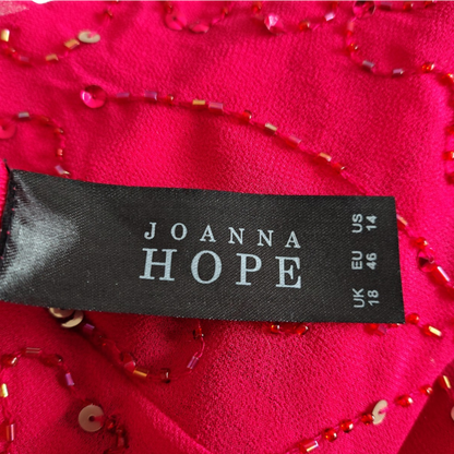 A close-up of a bright pink fabric garment with red and gold beaded trim and a black Joanna Hope brand label sewn onto the inside.